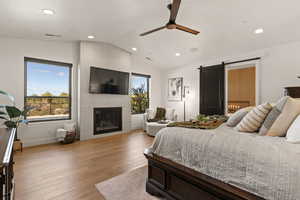 Bedroom with a barn door, vaulted ceiling, light wood-type flooring, a large fireplace, and recessed lighting