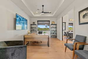 Office area with a raised ceiling, light wood-style floors, and ceiling fan