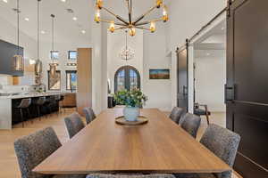 Dining area featuring a barn door, recessed lighting, a high ceiling, light wood-style flooring, and a chandelier