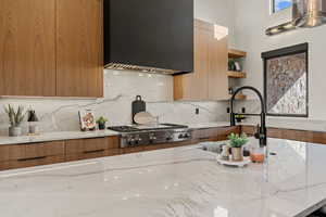 Kitchen featuring modern cabinets, light stone countertops, and custom exhaust hood