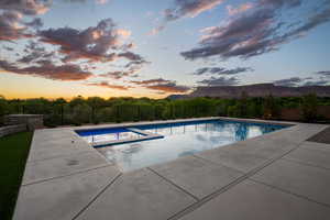 Pool at dusk with a fenced backyard, a patio, a pool with connected hot tub, and a mountain view