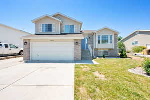 Split level home with concrete driveway, a garage, a front yard, and brick siding