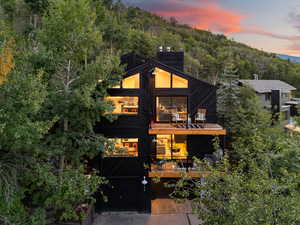 View of front of home with a balcony, a chimney, a forest view, concrete driveway, and a garage
