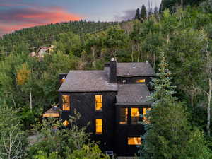 Rear view of property featuring a balcony, a forest view, a chimney, and a shingled roof