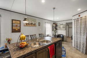 Kitchen featuring dark countertops, dishwasher, crown molding, pendant lighting, and light tile patterned floors
