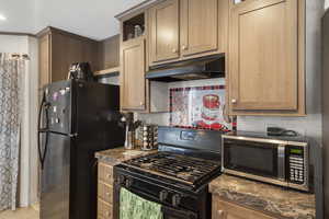 Kitchen featuring black appliances, under cabinet range hood, decorative backsplash, dark countertops, and open shelves