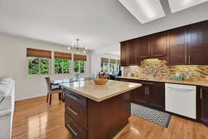 Kitchen with dishwasher, light wood-style floors, a chandelier, and decorative backsplash