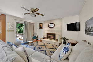 Living area featuring a ceiling fan, wood finished floors, and a brick fireplace