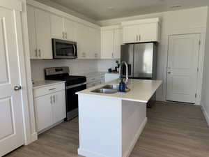 Kitchen with stainless steel appliances, light wood-style floors, white cabinets, and a center island with sink