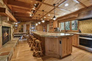 Kitchen with oven, a wood ceiling with exposed beams, light wood finished floors, a kitchen island, and a stone fireplace