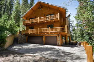 View of front facade featuring a balcony, driveway, a garage, and stone siding