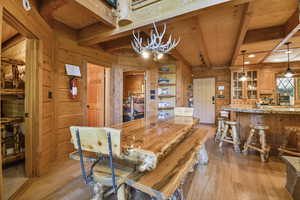 Dining room featuring wood walls, a wood ceiling with exposed beams, light wood finished floors, and a chandelier