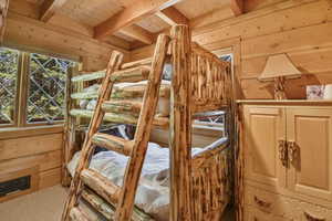 Unfurnished bedroom featuring a wood ceiling with exposed beams, wooden walls, and carpet