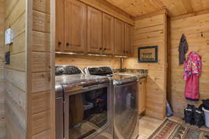 Washroom with washing machine and clothes dryer, cabinet space, wood walls, wooden ceiling, and light wood-style flooring