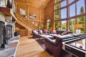 Living area with high vaulted ceiling, wooden walls, wood finished floors, a stone fireplace, and stairs