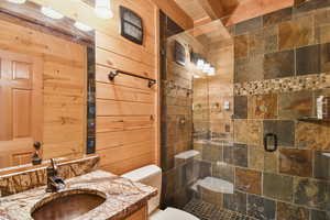 Full bath with vanity, a stall shower, and wooden walls
