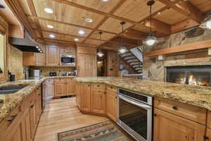 Kitchen with a wooden ceiling with exposed beams, light wood-style floors, appliances with stainless steel finishes, recessed lighting, and light stone counters