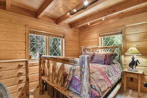 Carpeted bedroom featuring wood walls and a wood ceiling with exposed beams