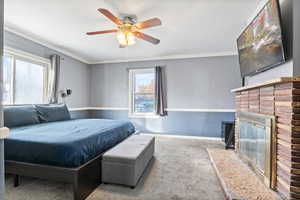 Bedroom #1 with a brick fireplace, carpeted flooring, crown molding, and a ceiling fan