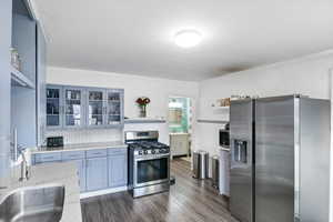 Updated Kitchen featuring grey cabinets, quartz countertops, stainless steel appliances, decorative backsplash, LVP flooring, and ornamental molding