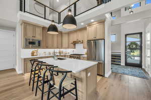 Kitchen with appliances with stainless steel finishes, a high ceiling, under cabinet range hood, light countertops, and a center island with sink