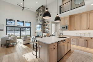 Kitchen featuring light brown cabinetry, appliances with stainless steel finishes, a towering ceiling, ceiling fan, and light wood-style floors