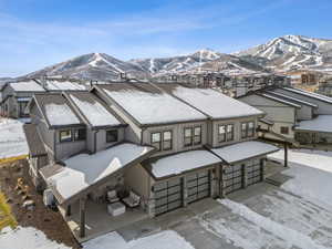 Snow covered house with a garage, a mountain view, and stone siding