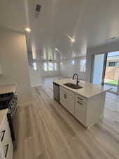 Kitchen featuring range with gas stovetop, white cabinetry, light LVP flooring, and an island with sink