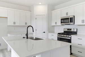 Kitchen with appliances with stainless steel finishes, a kitchen island with sink, white cabinetry, and light wood finished floors