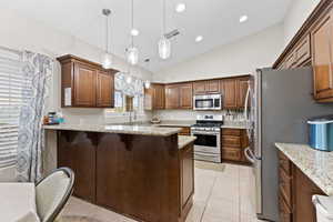Kitchen featuring appliances with stainless steel finishes, a kitchen breakfast bar, light stone countertops, a peninsula, and light tile patterned floors