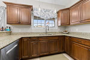 Kitchen with stainless steel dishwasher, decorative light fixtures, and light stone counters