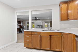 Kitchen featuring a ceiling fan, a desk, brown cabinetry, light tile patterned flooring, and light countertops