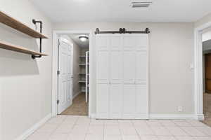 Unfurnished bedroom featuring light tile patterned flooring, a barn door, and light colored carpet