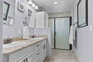 Bathroom featuring a textured wall, double vanity, and a stall shower