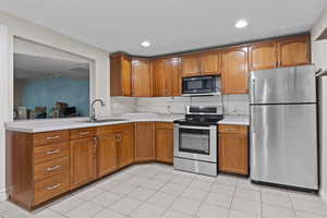 Kitchen featuring appliances with stainless steel finishes, brown cabinetry, light countertops, light tile patterned flooring, and recessed lighting