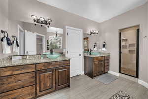 Full bath featuring a chandelier, a shower stall, and two vanities