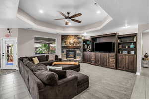 Living area with ceiling fan, a tray ceiling, a fireplace, and recessed lighting