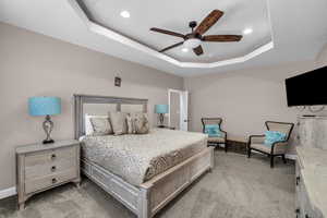 Bedroom with light colored carpet, a tray ceiling, recessed lighting, and ceiling fan