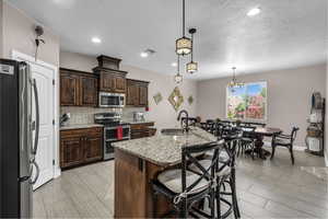 Kitchen featuring appliances with stainless steel finishes, tasteful backsplash, a breakfast bar area, light stone counters, and dark brown cabinetry