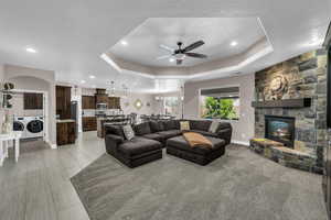 Living room featuring a ceiling fan, a stone fireplace, recessed lighting, a tray ceiling, and washer and clothes dryer