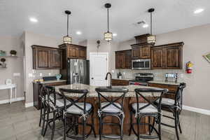 Kitchen with stainless steel appliances, dark brown cabinetry, decorative backsplash, recessed lighting, and a textured ceiling