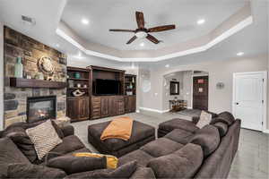 Living area with arched walkways, a ceiling fan, a tray ceiling, recessed lighting, and a fireplace