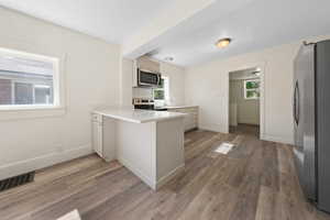 Kitchen with stainless steel appliances, a peninsula, light countertops, and light wood-style flooring