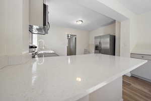 Kitchen featuring stainless steel fridge, a peninsula, light stone countertops, and wood finished floors