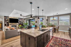 Kitchen with a textured ceiling, light wood-style floors, dark brown cabinetry, a stone fireplace, and a ceiling fan