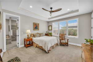 Bedroom featuring light carpet, a raised ceiling, recessed lighting, ensuite bath, and a ceiling fan