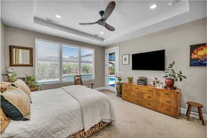 Bedroom with a tray ceiling, access to exterior, recessed lighting, light colored carpet, and a ceiling fan
