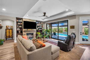 Living room featuring a stone fireplace, ceiling fan, light wood-style flooring, recessed lighting, and built in features