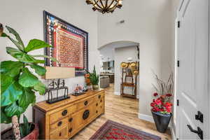 Entryway featuring arched walkways, light wood-type flooring, a chandelier, and a towering ceiling