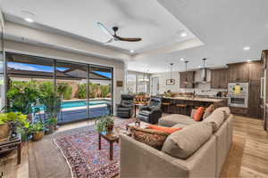 Living room with ceiling fan, light wood-type flooring, recessed lighting, and a raised ceiling